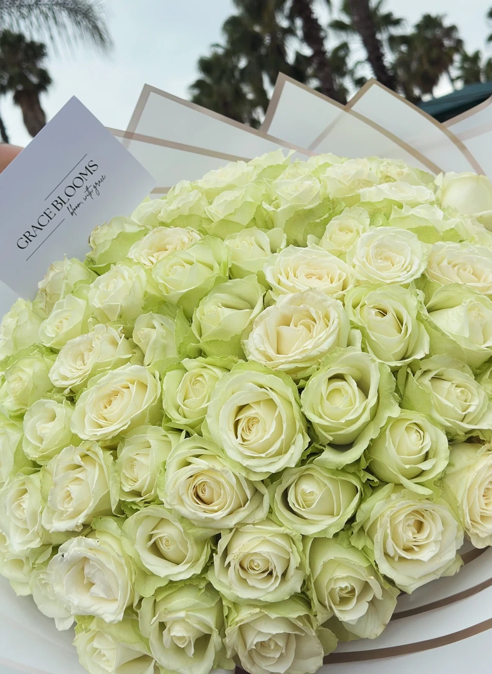 An abundant ivory rose bouquet in cream and gold-edged wrapping, with a Grace Blooms card