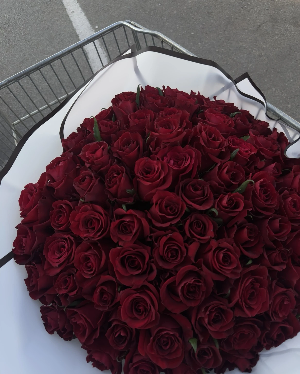 A generous red rose bouquet in white wrapping with a black edge